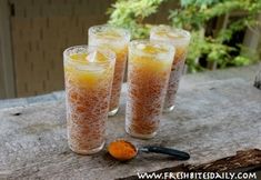 three glasses filled with orange liquid sitting on top of a wooden table next to an orange peel