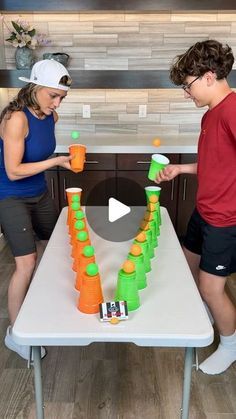 two people standing in front of a table with orange and green cups on it,