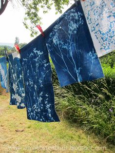 three blue and white towels hanging on a clothes line in front of some bushes with flowers