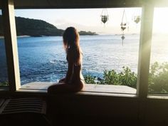 a woman sitting on top of a window sill looking out at the water and land