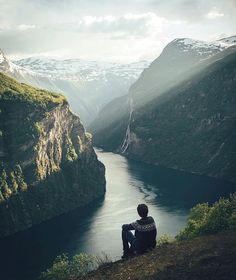 a man sitting on top of a cliff next to a river