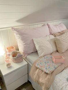 a white bed topped with lots of pillows next to a night stand and table lamp