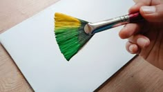 a hand holding a paintbrush with green, yellow and red bristles on it