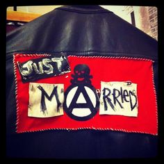 the back of a leather jacket with stickers and patches on it that says just anarchy