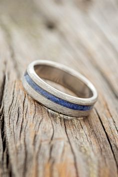 a silver ring with blue stripes sitting on top of a piece of wooden planks