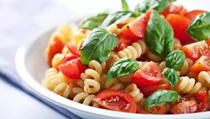 a white bowl filled with pasta salad and topped with tomatoes, green leafy leaves