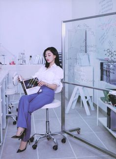 a woman sitting on a chair in an office holding a book and looking at the camera