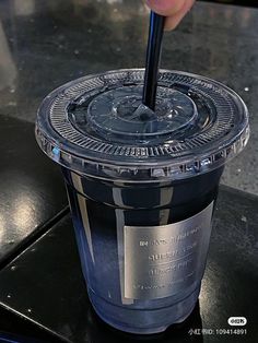 a person is holding a plastic cup with a black lid and straw in the middle