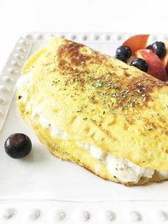 an omelet on a white plate with blueberries, peaches and strawberries