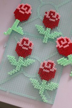 four pieces of beaded art with red flowers on green netted placemats