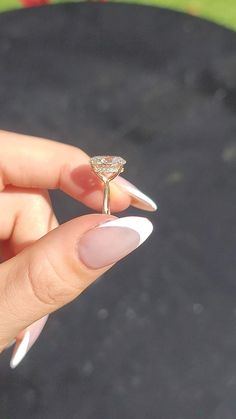 a woman's hand holding a gold ring with a diamond on it, in front of a black surface