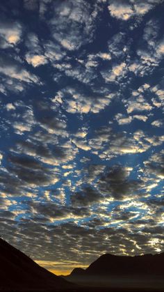 the sky is filled with clouds as the sun goes down in the mountains behind it