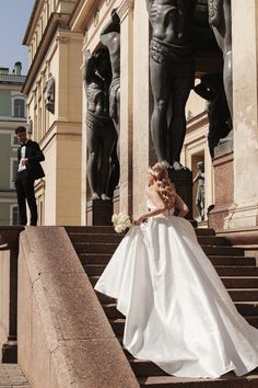 a woman in a white wedding dress sitting on some steps next to a large statue