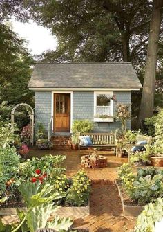 a small blue house surrounded by lots of plants and flowers in front of the door