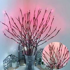 a vase filled with branches and lights on top of a white shelf next to a mirror