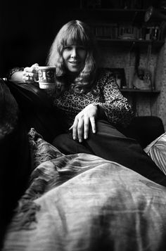 a black and white photo of a woman sitting on a bed holding a coffee cup