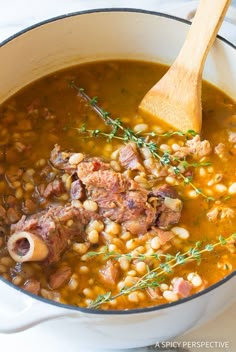 a pot filled with beans and meat next to a wooden spoon