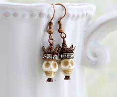 two skulls wearing crowns are hanging from the side of a white cup on a table