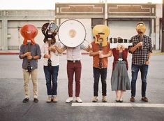 four people wearing masks and holding instruments in front of an empty parking lot with buildings behind them