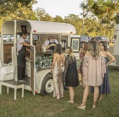 people are standing around in front of an ice cream truck that is parked on the grass