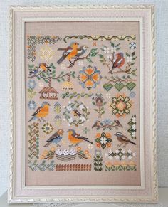 a cross stitch pattern with birds and flowers on the front, in a white frame