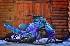 a purple and blue snowmobile parked in front of a wooden building with two doors