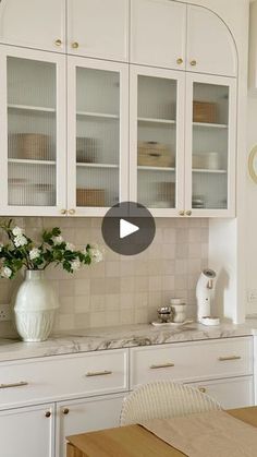 a kitchen with white cabinets and flowers on the counter top, in front of a window