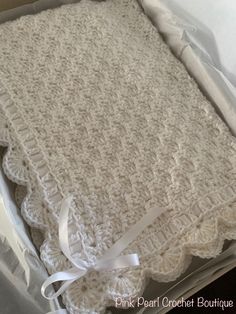 a crocheted blanket in a box with white ribbon on the bottom and side