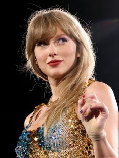 taylor swift performing on stage with her hand in the air and wearing a gold dress