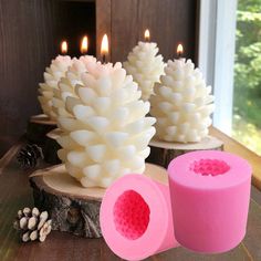 some candles are sitting next to each other on a table with pine cones in the background