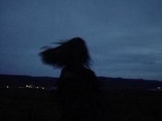 a blurry photo of a person standing in the dark with their hair blowing in the wind