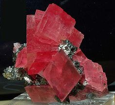 a cluster of red crystals sitting on top of a glass block in front of a window