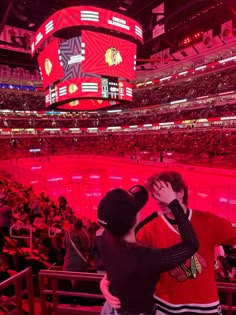 a man and woman standing next to each other in front of a hockey stadium filled with fans