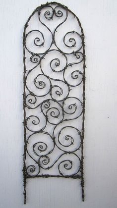 an iron wall hanging on the side of a white building with vines growing out of it