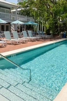 an empty swimming pool with lounge chairs and umbrellas near the side of the house