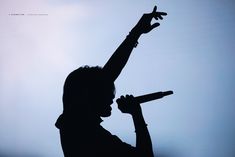 the silhouette of a person holding a microphone up in the air with their arm raised