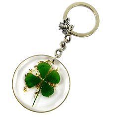 a four leaf clover on a white plate keychain with gold flakes around it