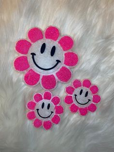 two pink flowers with smiley faces on them sitting on a white furnishing surface