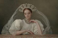 a woman wearing a tiara and veil sitting at a table with her hands on her chest