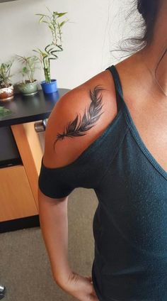 a woman with a feather tattoo on her upper arm and shoulder, standing in front of a desk