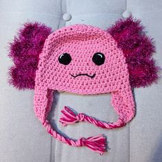 a crocheted pink hat with purple pom - poms