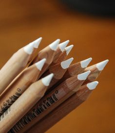 several pencils are lined up in a row on a wooden table, with the tops pointing upward