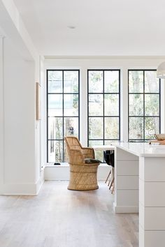 a kitchen with white walls and wooden floors has large windows that look out onto the backyard