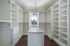 an empty walk - in closet with white cabinets and drawers, chandelier hanging from the ceiling