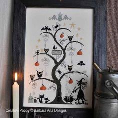 a cross - stitch halloween tree with cats and bats on it, next to a lit candle