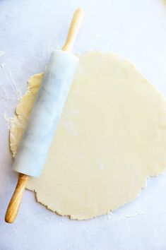 a rolling dough on top of a white counter next to a rolling pin and wooden handle