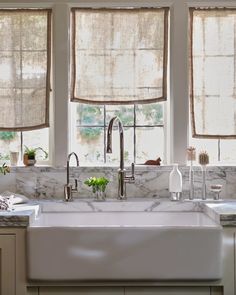 a kitchen with marble counter tops and white sink in front of two windows that have roman shades on them