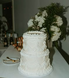 a white wedding cake sitting on top of a table next to a vase filled with flowers