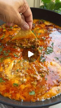 a person dipping tortilla chips into a skillet filled with meat and sauce