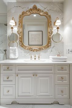 a white bathroom with gold accents and marble counter tops, an ornate mirror above the sink